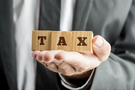 Close up Businessman Showing on his Palm Three Conceptual Wooden Blocks with TAX Word.