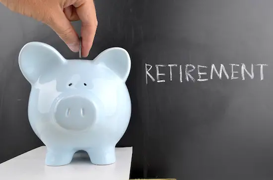 Image of a hand putting coin into a piggy bank with word 'retirement' on chalkboard in background