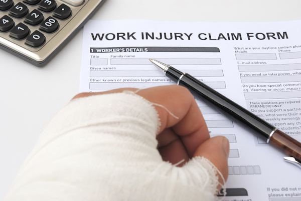 Image of an injured hand in a cast next to a work injury claim form on a desk