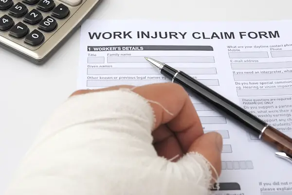 Image of an injured hand in a cast next to a work injury claim form on a desk