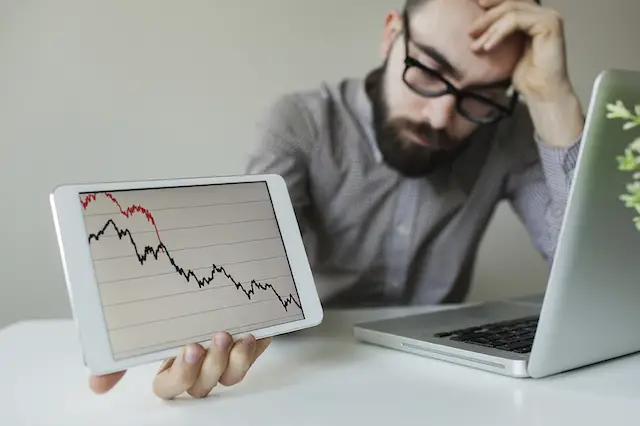 Depressed businessman leaning head below bad stock market chart in office