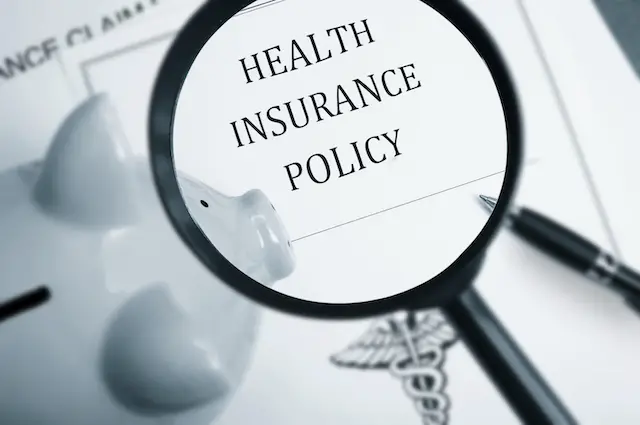 Magnifying glass over health insurance policy and piggy bank