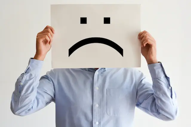 Businessman holding a poster board in front of his face with a sad face drawn on it