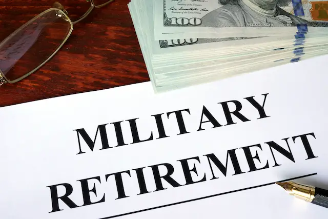 Words 'Military retirement' written on a paper on a desk next to a stack of dollar bills