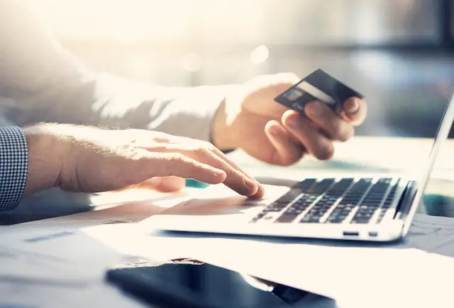 Image of a businessman using a credit card at a laptop to shop online