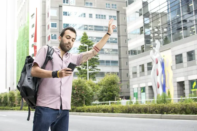 Image of man hailing a ride sharing service whilst holding a cellphone