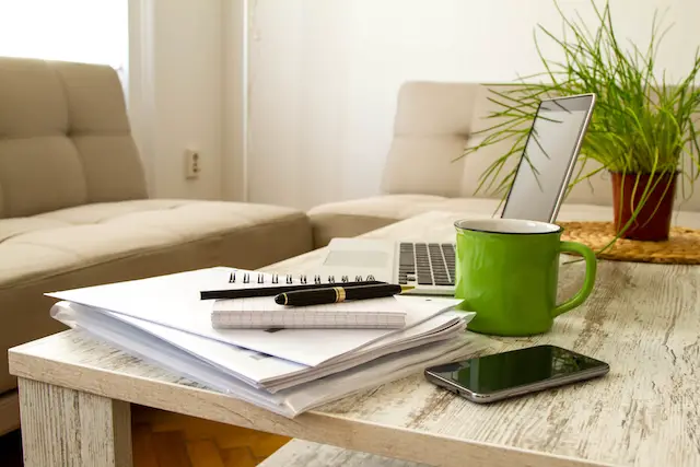 Image showing a telework setup with a laptop and stack of paperwork on a coffee table in front of a sofa