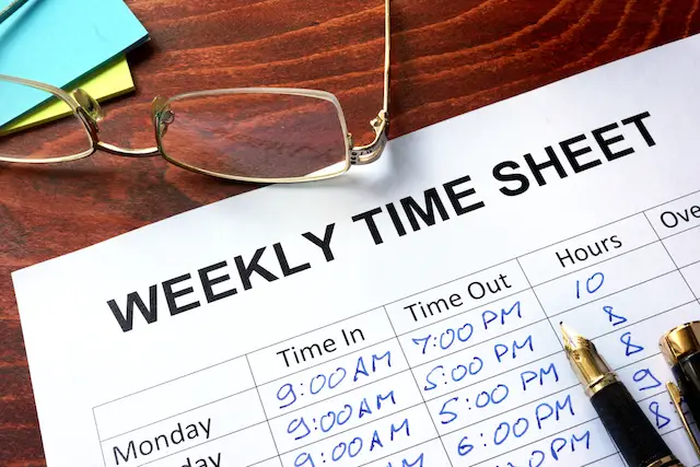 Image of a paper timesheet on a desk with a pair of glasses