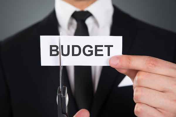 Businessman holding a piece of paper with the word 'budget' cutting it with scissors to illustrate budget cuts