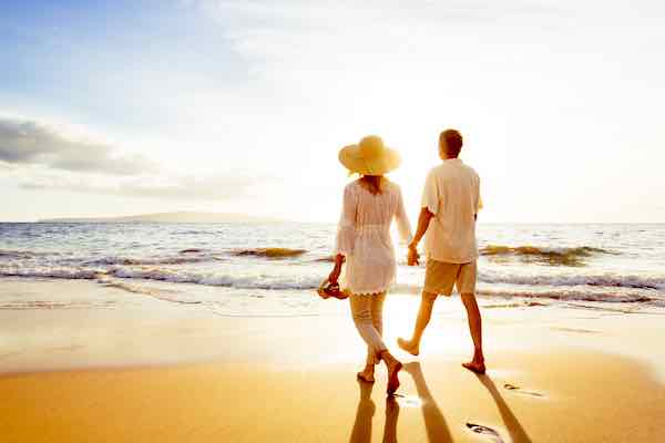 Retirement age couple walking on the beach at sunset