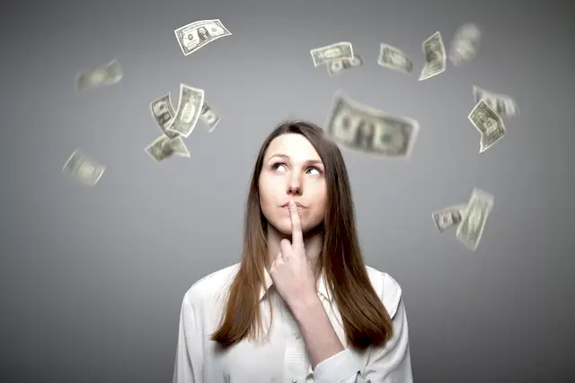 Young woman thinking about pay raise with dollar bills flying around her
