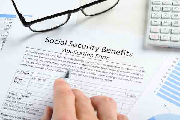 close-up of hand with pen and eyeglasses over social security benefits application form