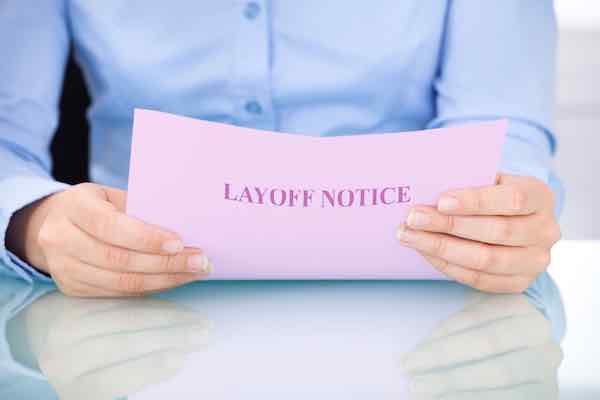 Businesswoman reading a document clearly labeled 'layoff notice' while sitting at her desk