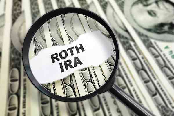 Words 'ROTH IRA' magnified under a magnifying glass on hundred dollar bills