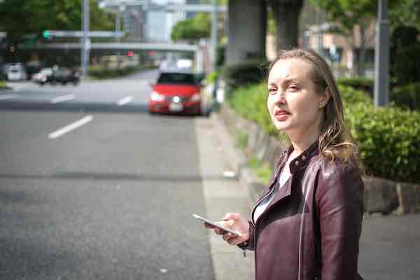 Young woman holding her cell phone and looking for a ride sharing service that she summoned