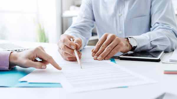 Close up of the hands of two businesspeople sitting at a desk and pointing at paperwork as they discuss what it says