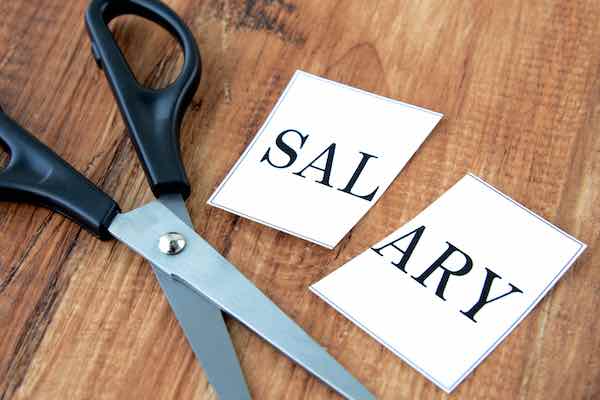 Scissors on a table lying next to the word 'salary' cut in half