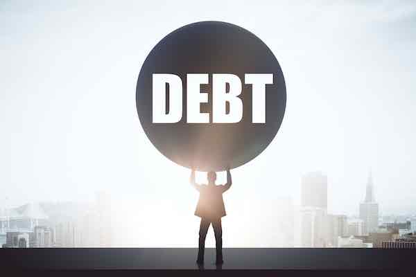 Struggling businessman holding a huge ball labeled 'debt'