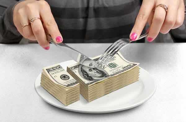 Hands cutting stack of $100 bills on a plate using a knife and fork
