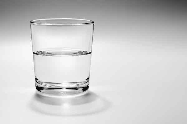 Half full, half empty glass of water on a white background with gray shadow