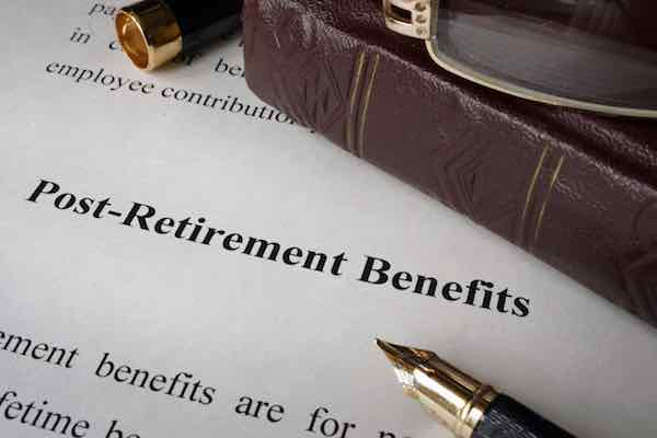 The words 'post-retirement benefits' on a sheet of paper next to books and a pen on an office table