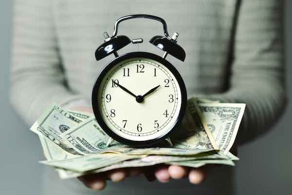 Closeup of a businessman holding an old style alarm clock sitting on top of a scattered pile of American dollars