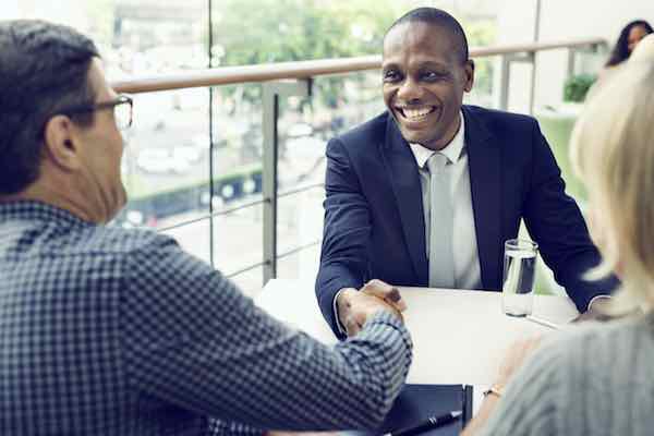 Man in business suit shaking hands with another man across the desk while his wife watches