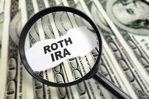 Words 'Roth IRA' magnified by a magnifying glass on top of hundred dollar bills