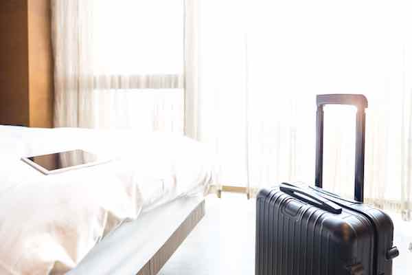 Suitcase in a hotel room along with an iPad on the hotel bed in the background