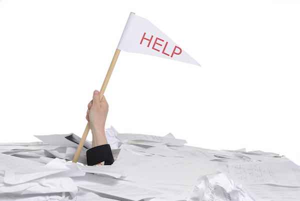 hand holding a flag with 'help' written on it, sticking out of a pile of papers