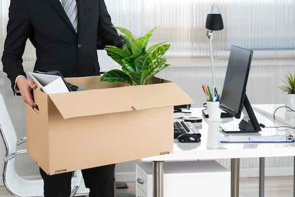 Midsection of businessman carrying cardboard box with his belongings by desk in office