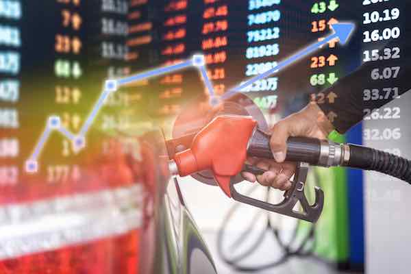 Close up of person's hand pumping gas into a car overlaid on a stock chart in the background