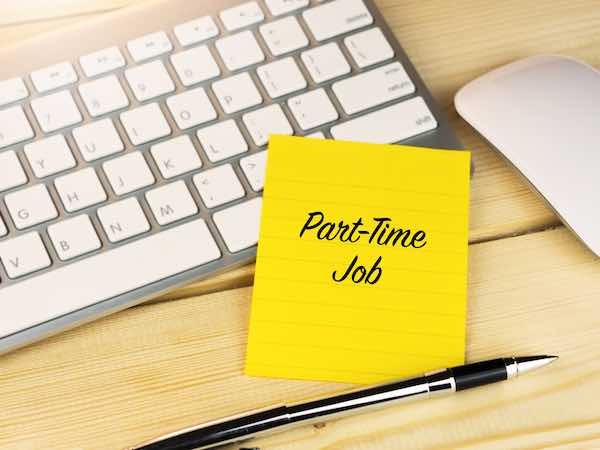 Words 'part time job' written on a yellow sticky note on a desk in front of a computer keyboard and mouse