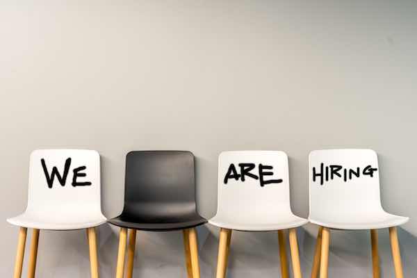 Words 'we are hiring' written on individual chairs setting in a horizontal row