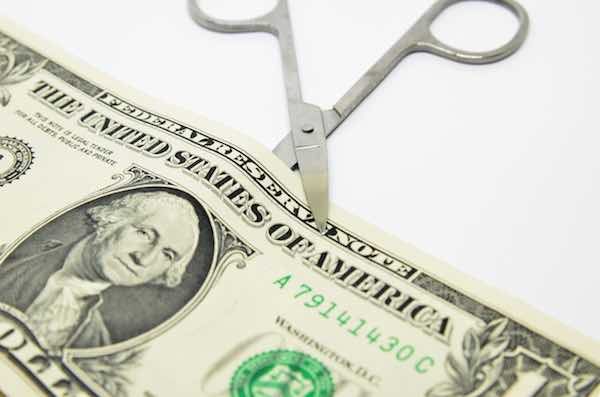 Scissors cutting through a dollar bill