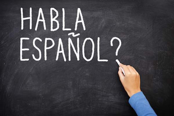 Teacher or student writing "habla espanol" on blackboard