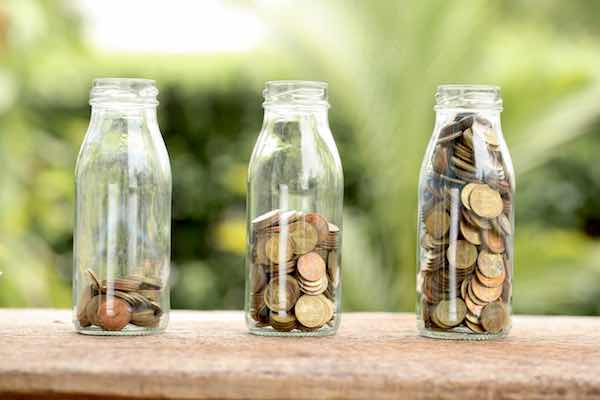 Three glasses in a row with increasing amounts of coins in them with the one on the left side filled with few coins and the one on the righthand side completely full