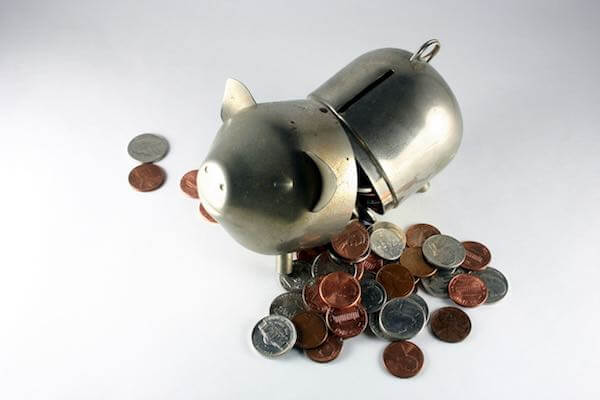 Image of a metal piggy bank opened in the middle separating it into two parts and spilling coins out onto a solid white surface depicting withdrawing savings