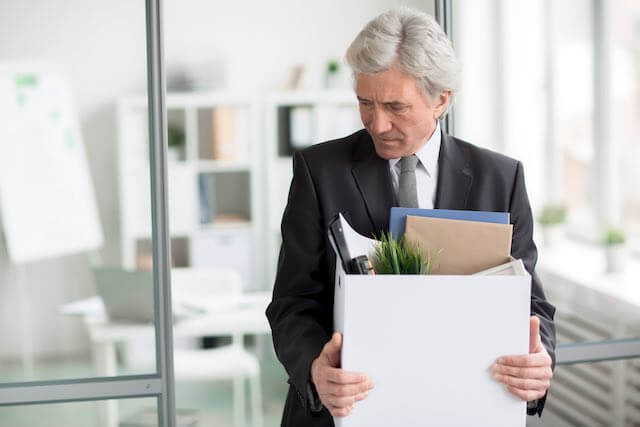 Middle aged businessman holding a box of personal belongings as he leaves his office depicting resignation or job loss