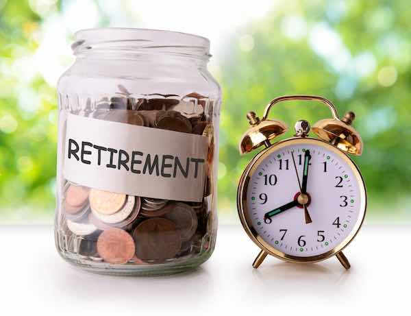 Coins in a glass jar labeled 'retirement' sitting next to a retro alarm clock