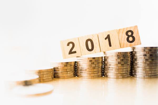 Numbers '2018' on individual wooden blocks balanced on several increasingly high stacks of coins signifying a 2018 pay raise