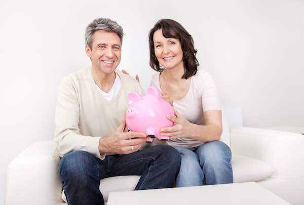 Mature couple holding a piggy bank together while sitting next to each other on the couch