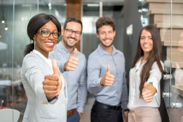 Group of four happy business people giving a thumbs up