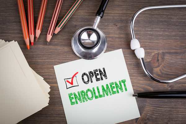 Paper reading 'open enrollment' lying on a desk next to a stethoscope and pencils