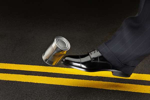 close up of politician's shoe kicking a dented shiny can down the road