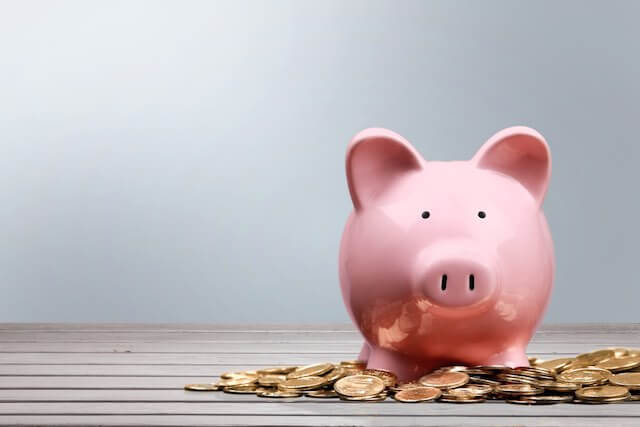 Pink piggy bank surrounded by a small scattering of gold coins on a wooden tabletop