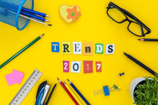 Individual cutout letters spelling 'trends 2017' on a yellow desk background surrounded by glasses, paintbrushes, pencils and ruler