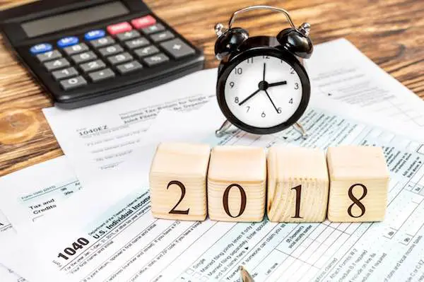 Wooden cubes with numbers "2018" sitting on top of a series of tax forms alongside a calculator