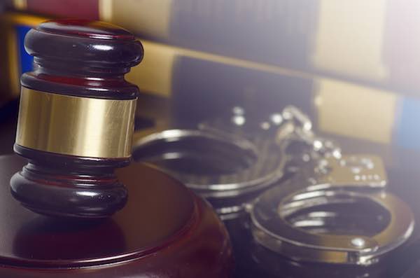 Judge's gavel sitting on a desk with a pair of handcuffs in the background