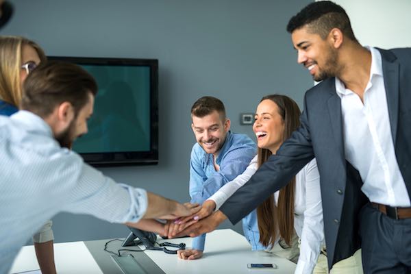 Group of happy co-workers joining their hands over a conference room table in a show of teamwork/unity